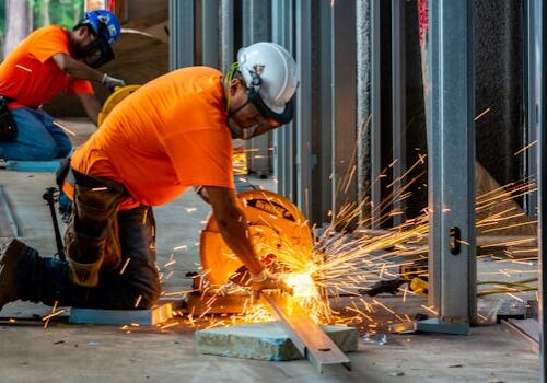 Workers cutting metal beams with a grinder, creating sparks inside a construction site.